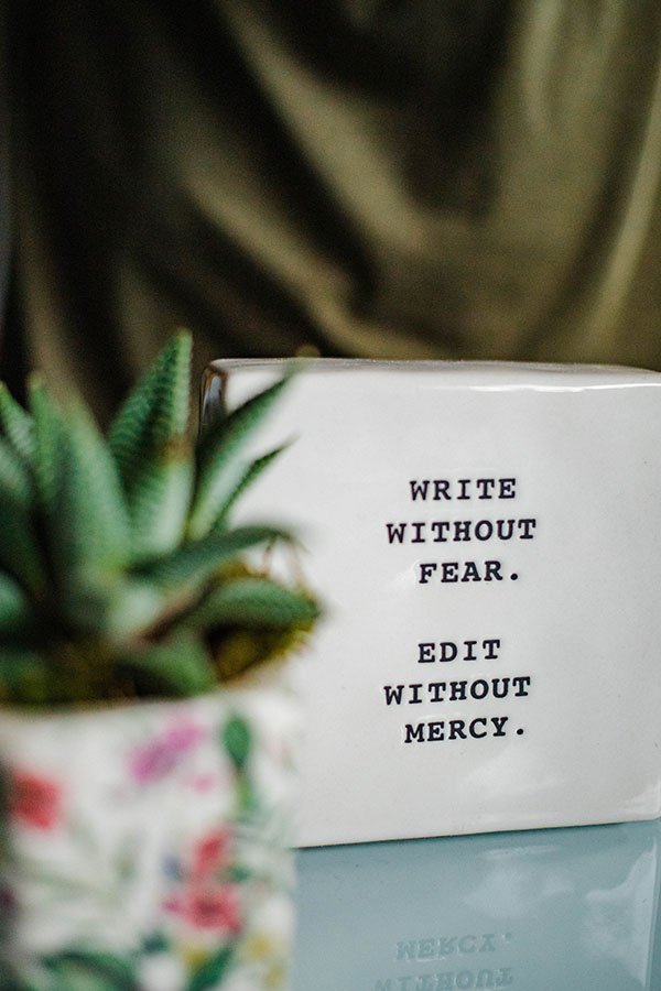 Blogging 101, reads write without fear. Edit without mercy on a ceramic tile with an unfocused potted plant in the foreground.